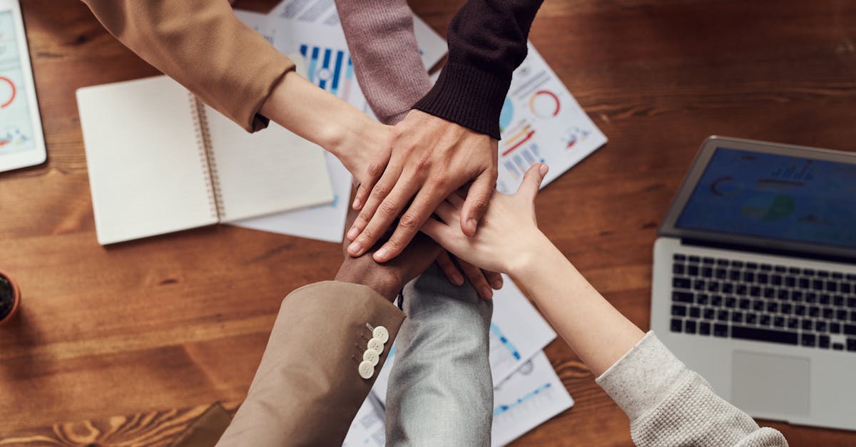 Diverse professionals unite for teamwork around a wooden table with laptops and documents.